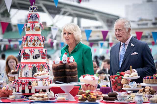 Carlos y Camilla ante una mesa repleta de fresas, dulces y una tarta de siete pisos decorada con símbolos de Londres y de la reina.