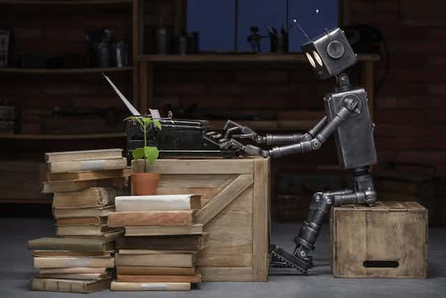 Un robot sentado sobre una caja de madera escribe en una máquina de escribir rodeado de libros.