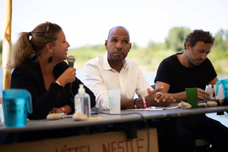 Three people sit at a table outdoors.