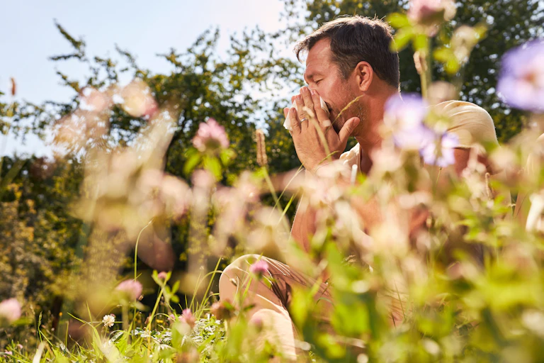 A man sitting in a flowering garden blows his nose.
