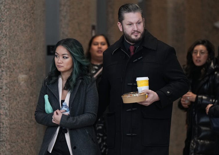A man and woman walk out of a courthouse. The man is carrying a coffee cup.