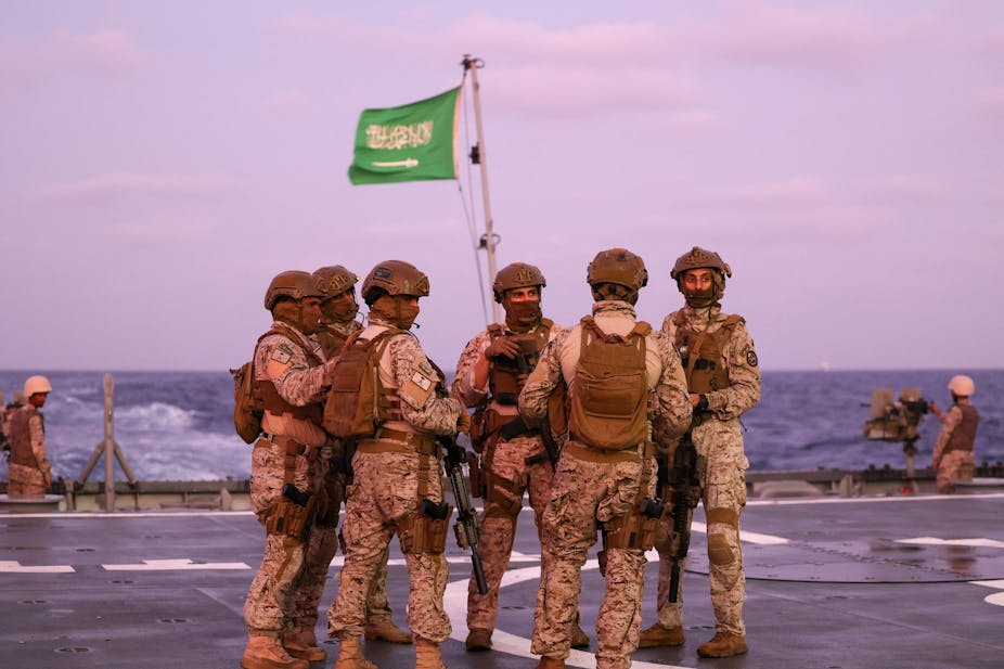 A group of men standing on board a military vessel with a flag hoisted on its mast.
