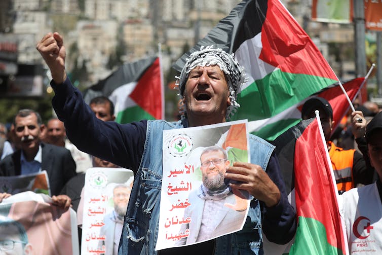 An eldlerly woman shakes her fist and shouts while holding up a picture of Khader Adnan who died in Israeli custody following a hunger strike.