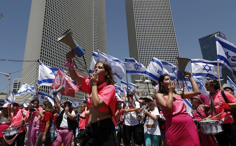 Israeli protesters hold up banners and shout through megaphones during mass protests in Tel Aviv.
