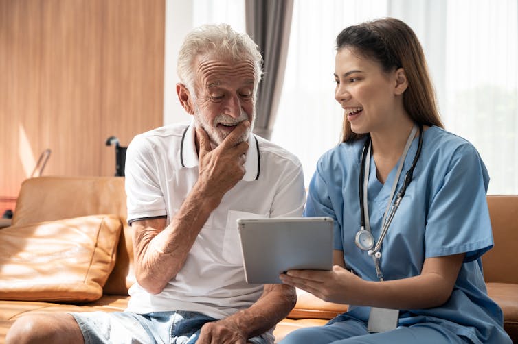 senior man sitting in chair and talking with a health-care provider wearing scrubs and a stethoscope