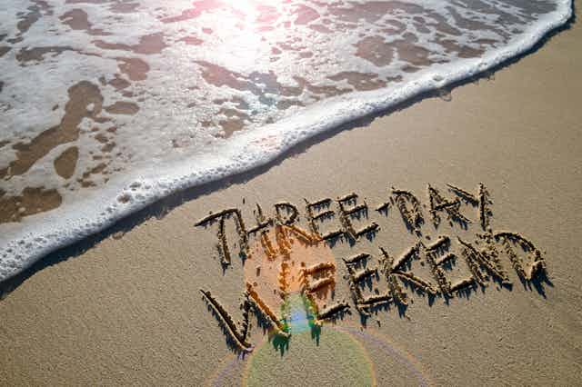 Beach picture with "Three-day weekend" written in sand with the tide coming in.