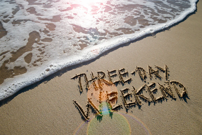 Beach picture with "Three-day weekend" written in sand with the tide coming in.
