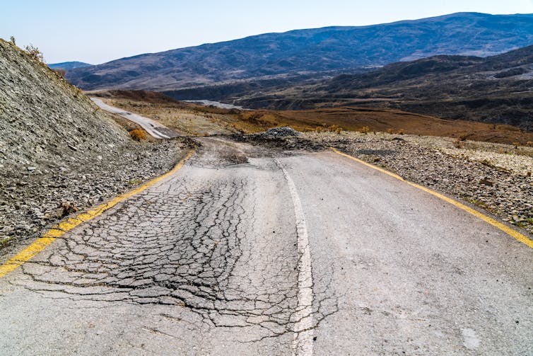 Surrounded by hills and mountains is an isolated two-lane road, cracked and crumbling.