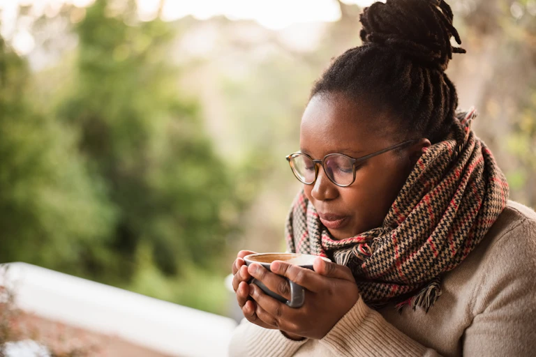 A young woman wearing a heavy scarf cups a cup of coffee in her hands