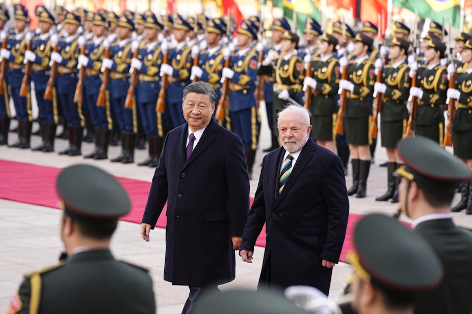 Two men wearing dark coats, president Xi and president Lula, in front of a line of soldiers.