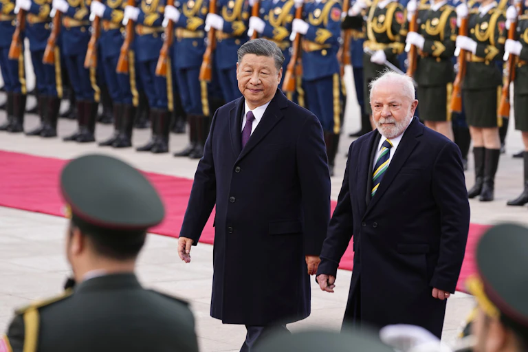 Two men wearing dark coats, president Xi and president Lula, in front of a line of soldiers.