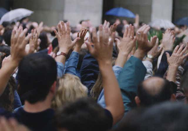 Gente de espaldas en una manifestación alzando las manos.