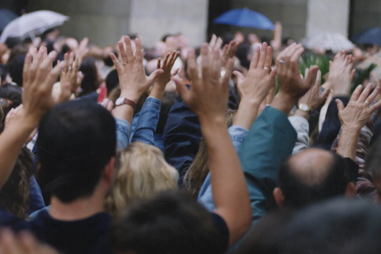 Gente de espaldas en una manifestación alzando las manos.