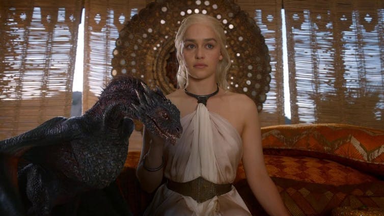 Una mujer sentada con un dragón pequeño al lado.