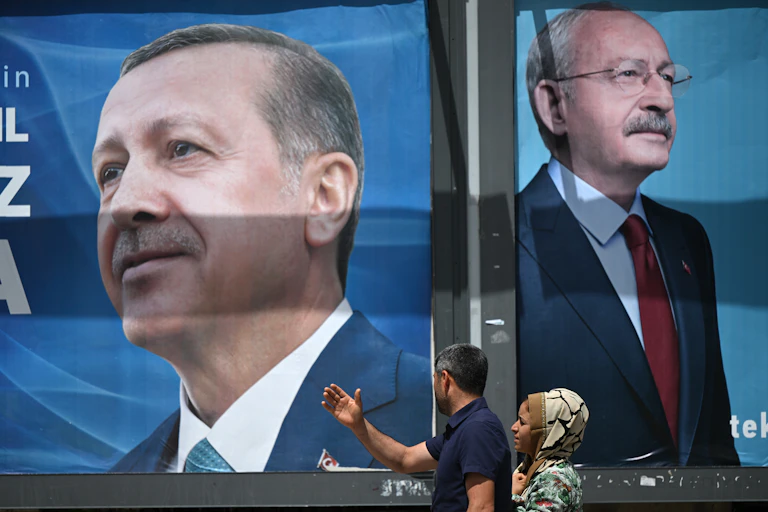 Un couple passe devant des panneaux d'affichage portant le portrait du président turc Recep Tayyip Erdogan (à gauche) et celui du leader du Parti républicain du peuple (CHP) et candidat à la présidence, Kemal Kilicdaroglu (à droite), à Sanliurfa, dans le sud-est de la Turquie, le 28 avril 2023.