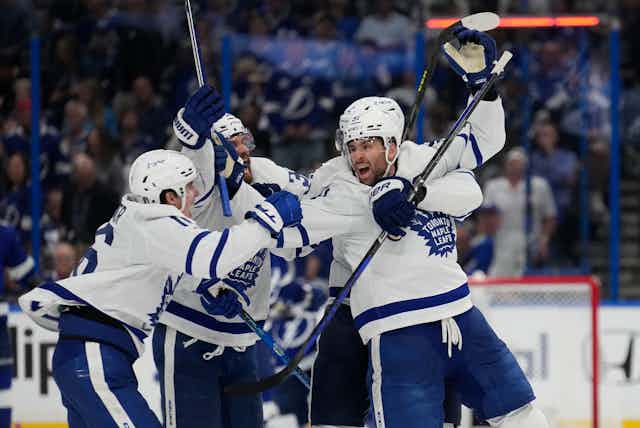 A group of hockey players in blue and white uniforms with the Toronto Maple Leafs logo on them hug each other in celebration
