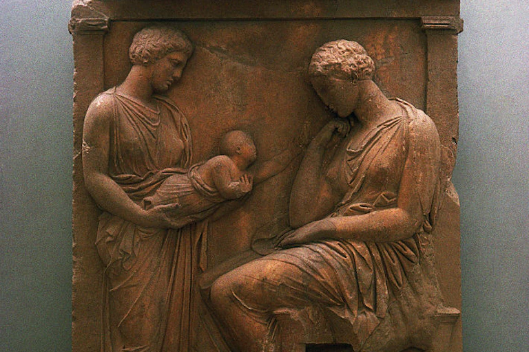 A carved relief shows two women looking at a baby that one of them is holding.