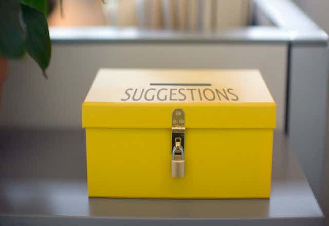 a yellow box with a slit and the word suggestions on it sits on a table