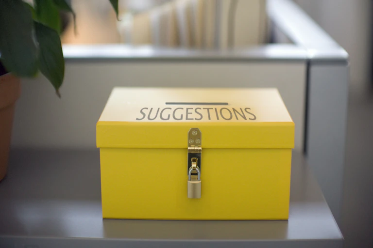 a yellow box with a slit and the word suggestions on it sits on a table
