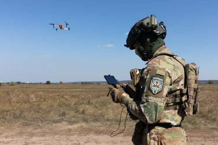 Un militar opera un mando que tiene en las manos y que dirige la trayectoria de un dron.