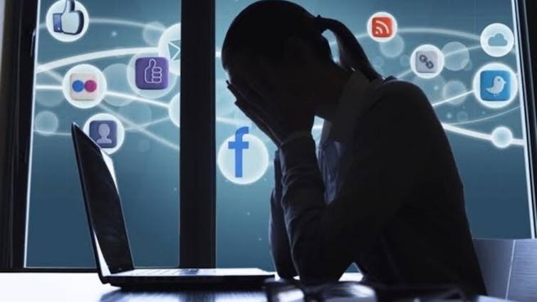 La silueta de una mujer que se tapa la cara frente a un ordenador mientras los logotipos de diferentes redes sociales la rodean.