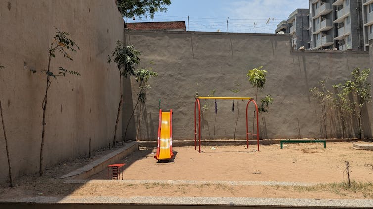 Sandy area with a yellow slide surrounded by high walls painted grey topped with barbed wire.