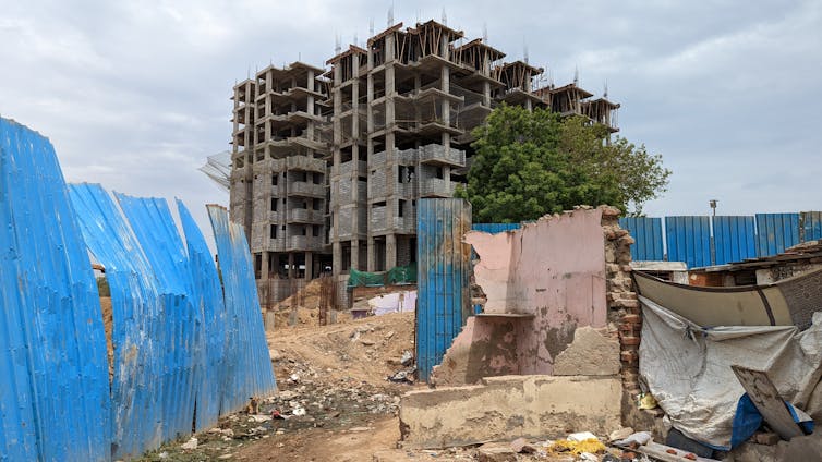 Demolished houses in foreground with sheet metal fence separating street from construction site