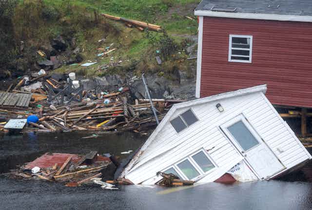 Damaged buildings and debris surrounded by water near a shoreline. 