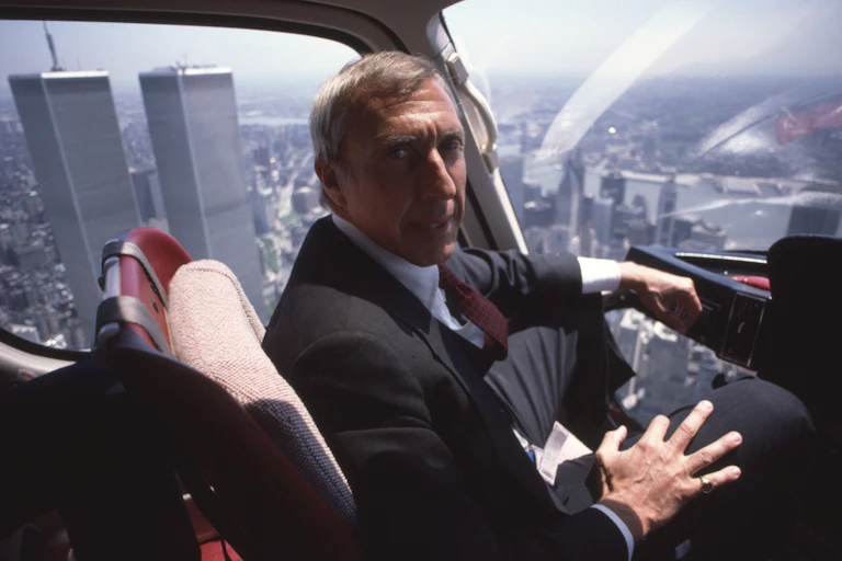 an older man in a suit rides in an aircraft over Manhattan