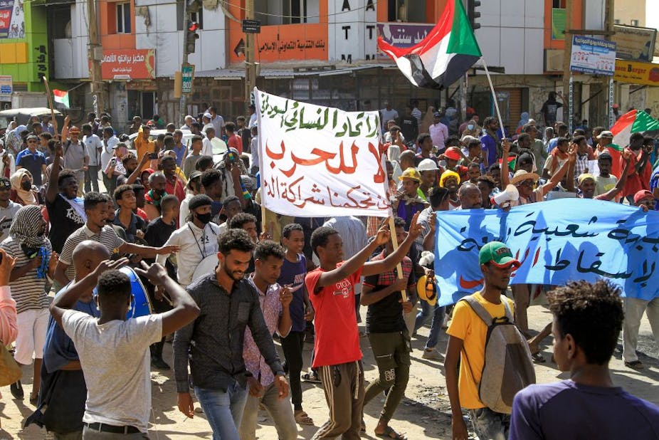 A group of people walking along a street holding up banners and the Sudanese flag