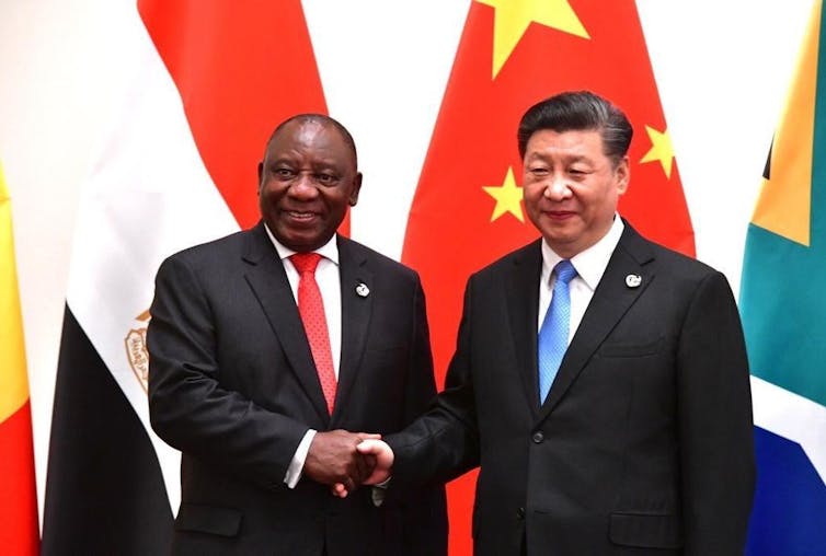 Two men shake hands in from of Chinese and South African flags.