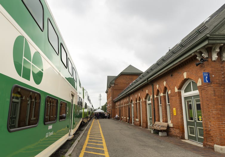 A green and white double-decker train sits at a red brick train station.