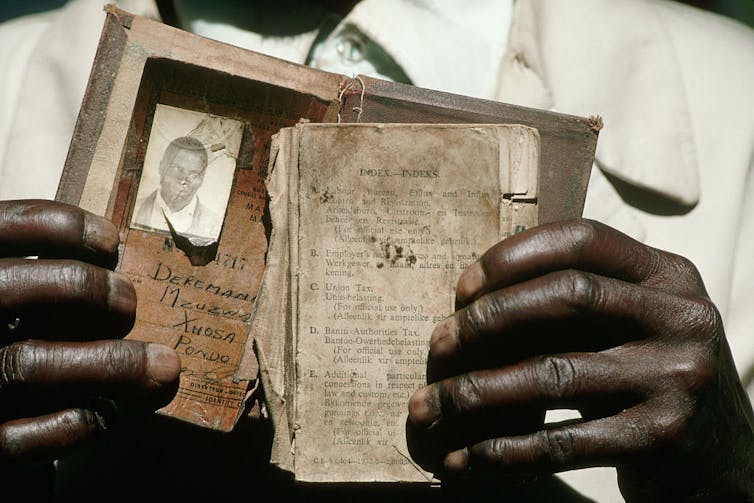Close up of hands holding an old, battered document containing an identity photo and personal information.