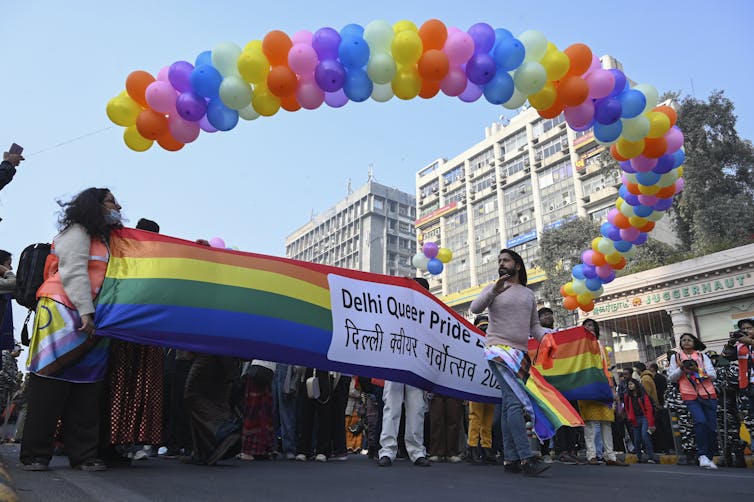 People at a march with rainbow coloured balloons and a banner that reads: Delhi queer pride.