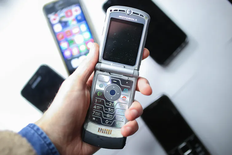 Une personne tenant un téléphone portable à clapet au-dessus d’une table couverte d’un assortiment de smartphones