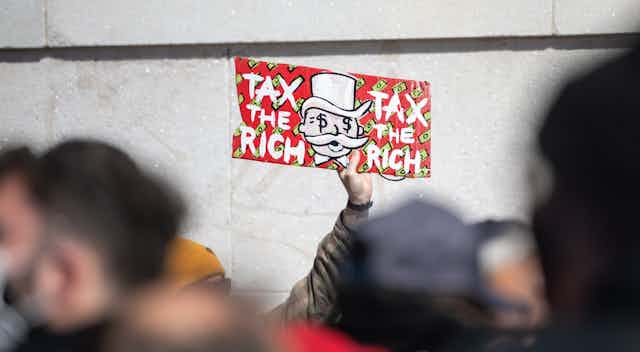 A person holds up a sign that says Tax the Rich at a protest.