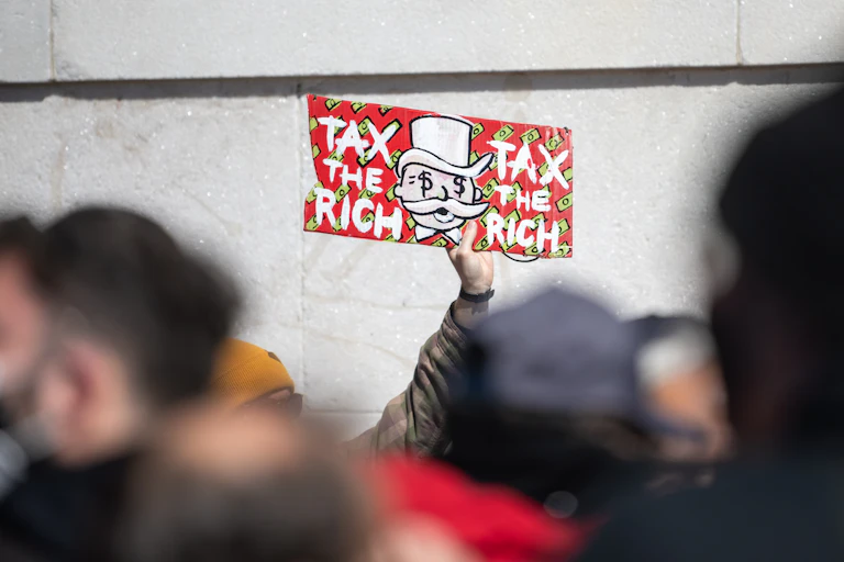 A person holds up a sign that says Tax the Rich at a protest.
