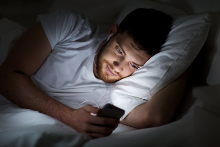 A man looking at a smartphone while lying in bed