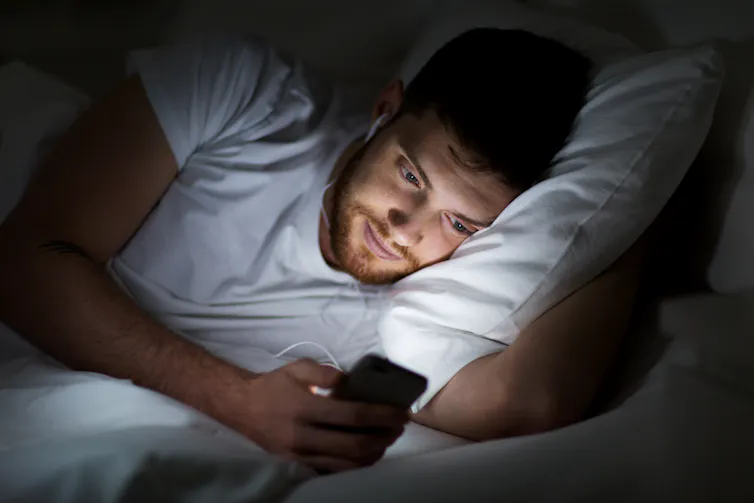 Un homme regardant un smartphone alors qu’il est allongé dans son lit