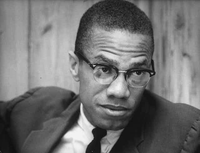 A bespectacled Black man wearing a  coat and a tie.