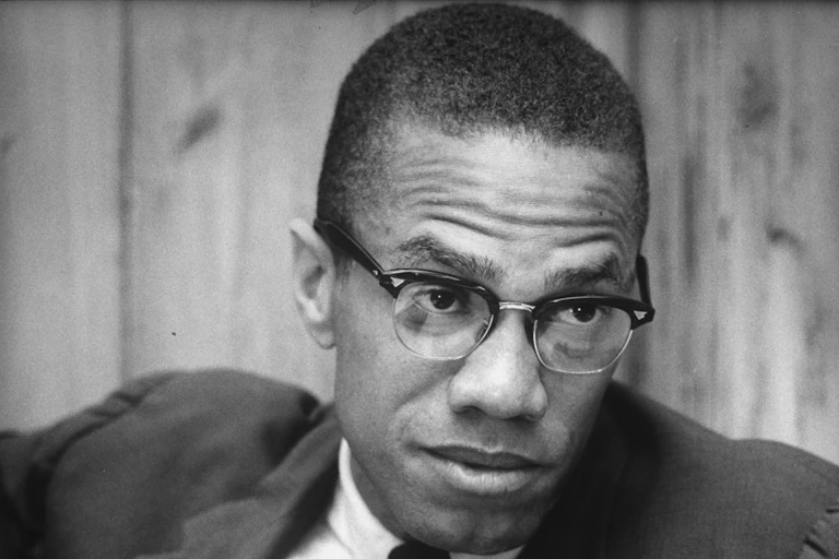 A bespectacled Black man wearing a coat and a tie.