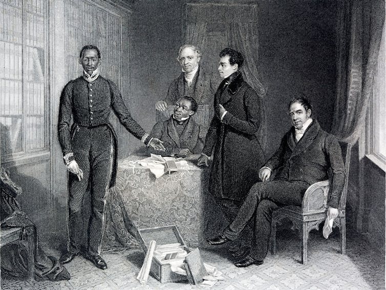 A vintage illustration in black and white of an African man in formal western attire standing next to a table where three other men stand and sit in a lavish drawing room.
