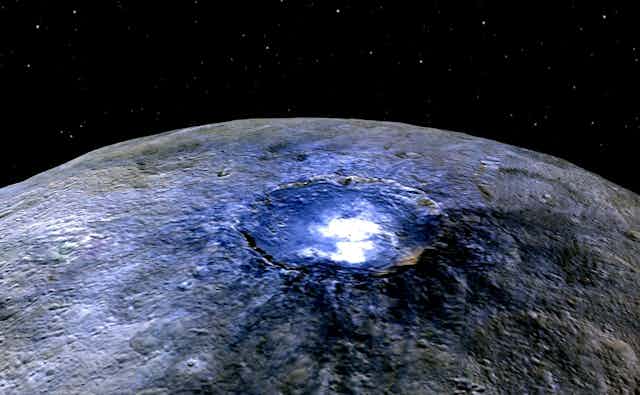 A blue and white glowing crater on a grey rock on a star field background