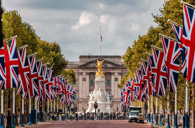 View of Victoria fountain and Buckingham Palace from the mall, which is lined with Union Jack flags on either side