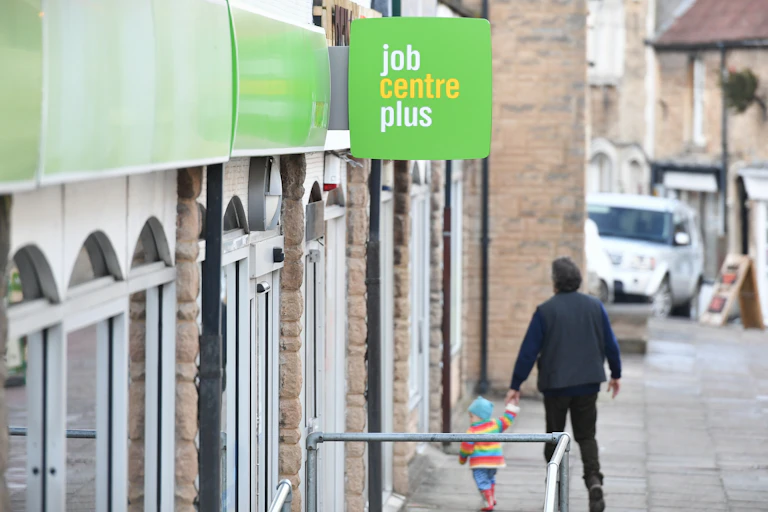Man holding child's hand walking past a "Job Centre Plus" shopfront.