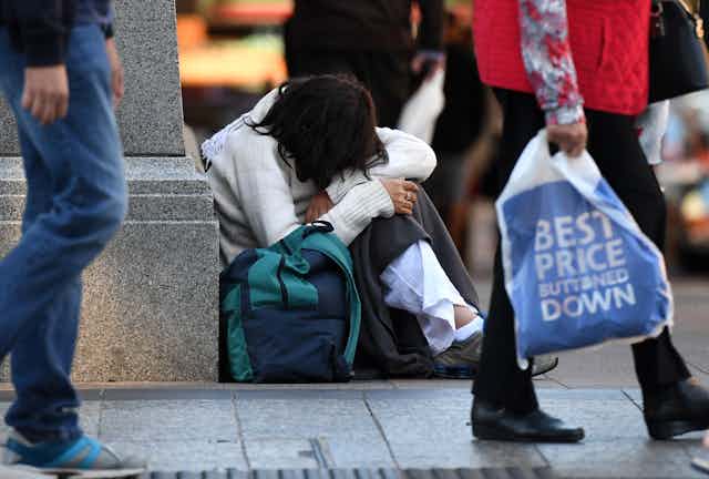 Woman sits on the floor with a bag while shoppers walk past