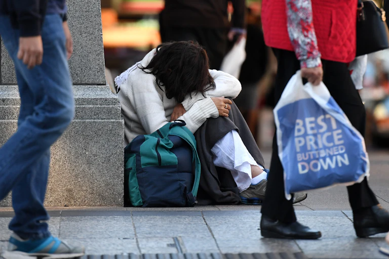 Woman sits on the floor with a bag while shoppers walk past