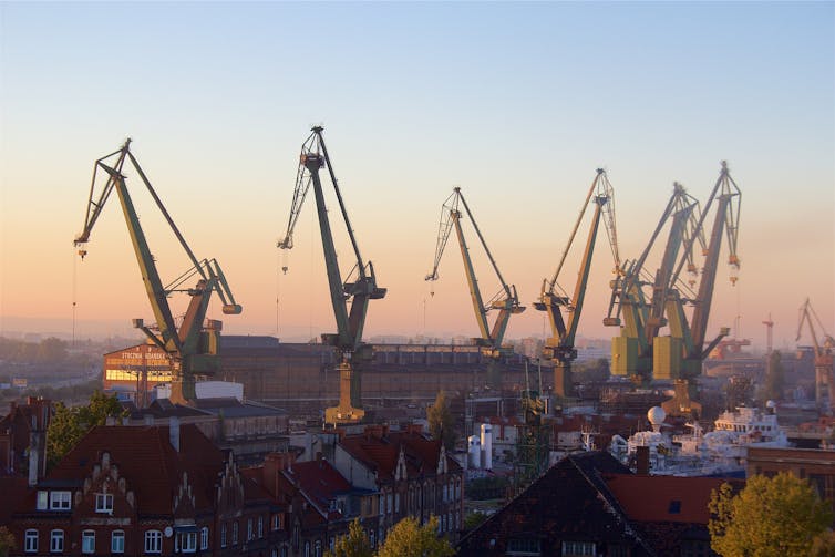 Giant shipyard cranes seen on the horizon at dusk.