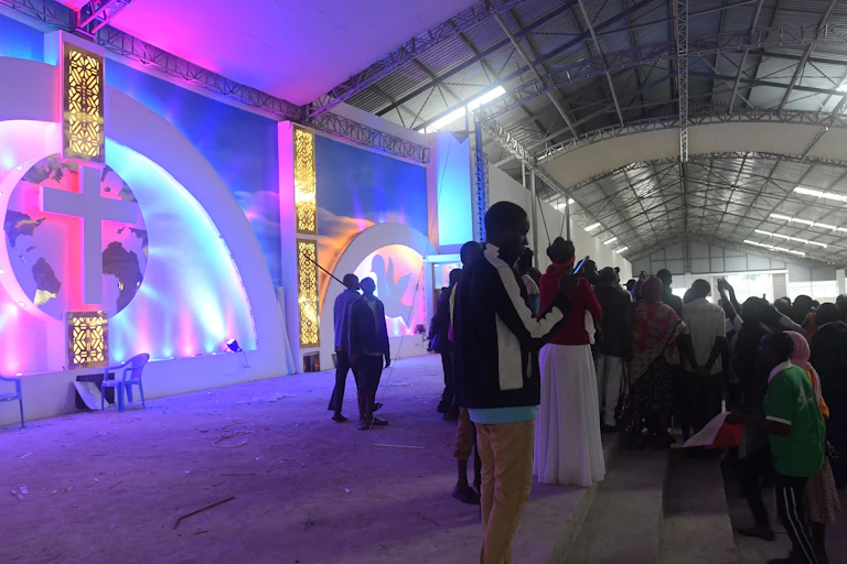 People gather in front of a stage with a cross