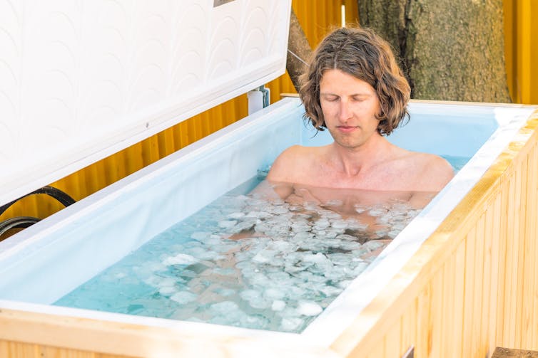 Niño u hombre con los ojos cerrados bañándose en el agua fría entre cubitos de hielo